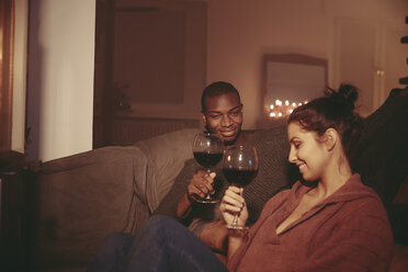 Happy young woman toasting with red wine in the living room - FMKF03420