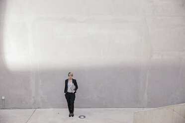 Geschäftsfrau mit Laptop vor einer Betonwand stehend - FMKF03426