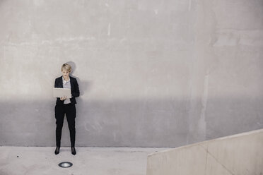 Geschäftsfrau steht vor einer Betonwand und benutzt einen Laptop - FMKF03427