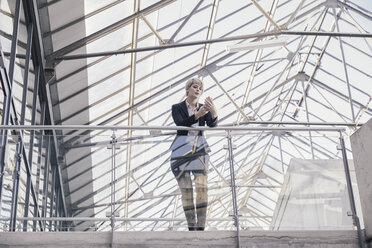 Businesswoman looking at smartphone in modern architecture - FMKF03431