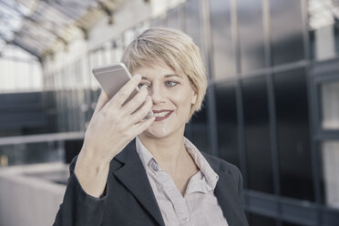 Porträt einer lächelnden blonden Geschäftsfrau, die ein Mobiltelefon hält - FMKF03437