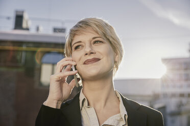 Porträt einer lächelnden blonden Geschäftsfrau am Telefon bei Gegenlicht - FMKF03440