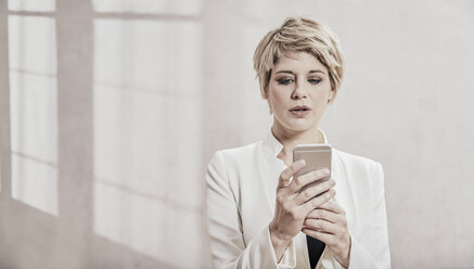 Porträt einer blonden Geschäftsfrau, die auf ihr Handy schaut - FMKF03442