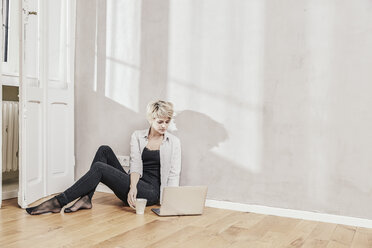 Frau auf dem Boden sitzend mit Kaffeetasse und Laptop - FMKF03443