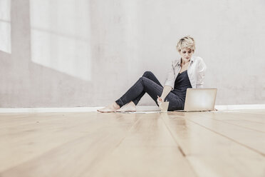 Frau auf dem Boden sitzend mit Kaffeetasse und Laptop - FMKF03444