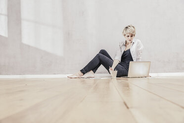 Woman sitting on the floor with coffee cup using laptop - FMKF03444