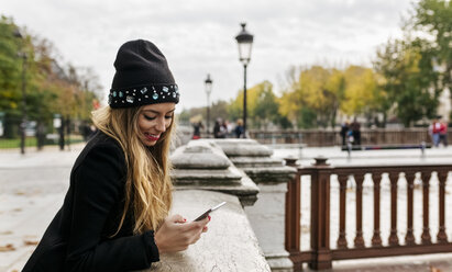 Frankreich, Paris, lächelnde junge Frau, die auf ihr Mobiltelefon schaut - MGOF02730