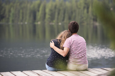 Rückenansicht eines jungen Paares, das auf einem Steg am See sitzt - HAPF01292