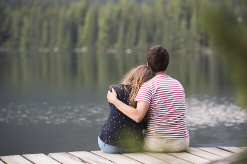 Rückenansicht eines jungen Paares, das auf einem Steg am See sitzt - HAPF01292