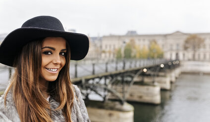 France, Paris, portrait of smiling young woman wearing black hat near River Seine - MGOF02742