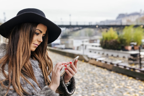 Frankreich, Paris, Porträt einer jungen Frau, die in der Nähe der Seine ein Mobiltelefon benutzt, lizenzfreies Stockfoto