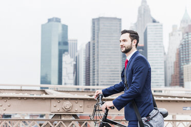 USA, New York City, Geschäftsmann mit Fahrrad auf der Brooklyn Bridge - UUF09634