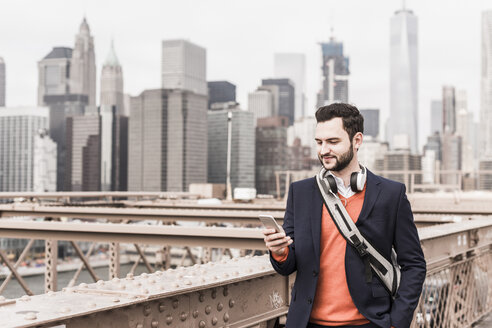 USA, New York City, Mann auf der Brooklyn Bridge, der ein Mobiltelefon benutzt - UUF09660