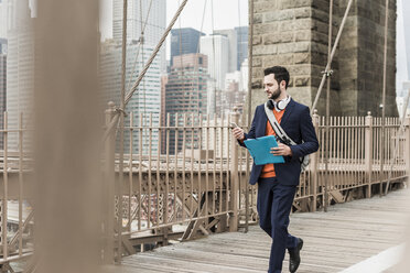 USA, New York City, Mann geht auf der Brooklyn Bridge und benutzt ein Mobiltelefon - UUF09661