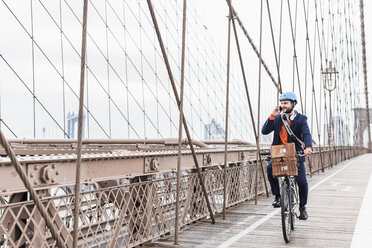 USA, New York City, Mann auf dem Fahrrad auf der Brooklyn Bridge mit Mobiltelefon - UUF09664