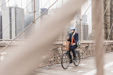 USA, New York City, man on bicycle on Brooklyn Bridge using cell phone - UUF09666