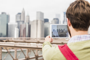 USA, New York City, Mann auf der Brooklyn Bridge beim Fotografieren mit dem Tablet - UUF09668