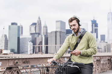 USA, New York City, man on bicycle on Brooklyn Bridge using cell phone - UUF09672