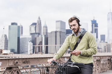 USA, New York City, Mann auf dem Fahrrad auf der Brooklyn Bridge mit Mobiltelefon - UUF09672