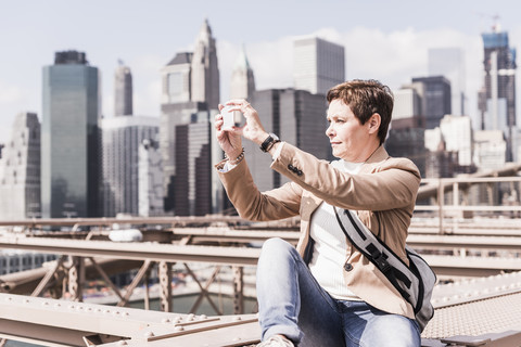 USA, New York City, Frau auf der Brooklyn Bridge beim Fotografieren mit dem Handy, lizenzfreies Stockfoto
