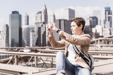 USA, New York City, Frau auf der Brooklyn Bridge beim Fotografieren mit dem Handy - UUF09677