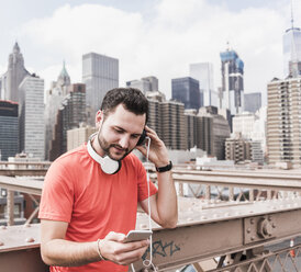 USA, New York City, athlete on Brooklyn Brige with cell phone and headphones - UUF09687