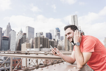 USA, New York City, athlete on Brooklyn Brige with cell phone and headphones - UUF09688