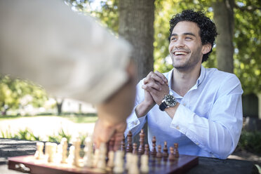 Glücklicher junger Mann spielt eine Partie Schach im Park - ZEF12315