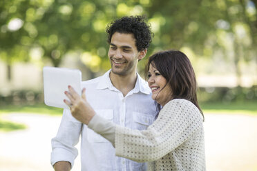 Smiling mother and adult son looking at tablet in park - ZEF12332