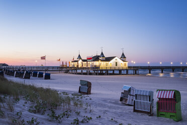 Germany, Usedom, Ahlbeck, view to lighted sea bridge with hooded beach chairs in the foreground at dusk - SIEF07233