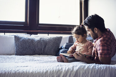 Father and daughter reading book, lying on bed - WESTF22435