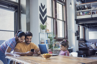 Familie sitzt in der Küche, Eltern benutzen ein Smartphone, Tochter schaut auf den Laptop - WESTF22443