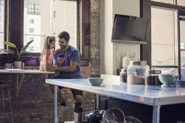 Father with daughter using smart phone in kitchen - WESTF22491