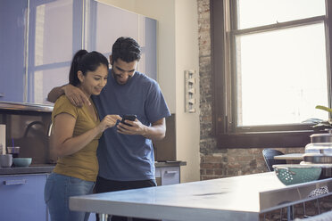 Young couple in kitchen using smart phone - WESTF22505