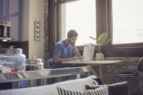 Young man standing in kitchen using laptop stock photo