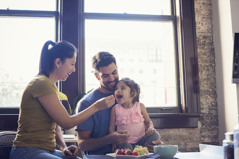 Mother and father feeding their little daughter in kitchen stock photo