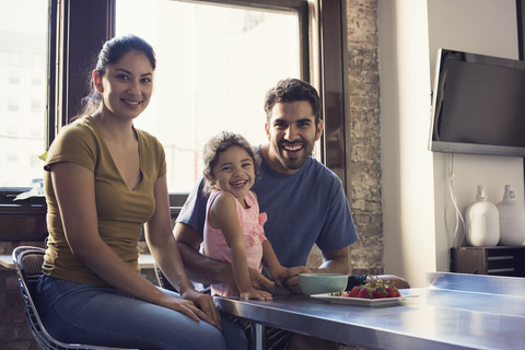 Familie sitzt in der Küche und schaut in die Kamera, lizenzfreies Stockfoto