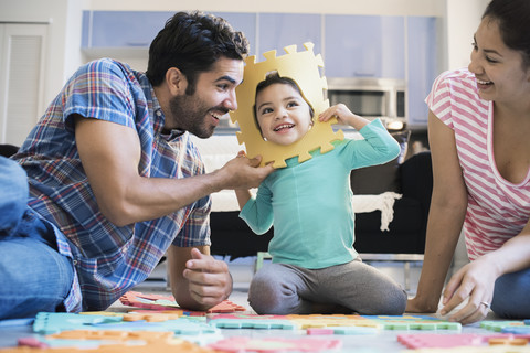 Glückliche Familie sitzt auf dem Boden und spielt mit ihrer Tochter, lizenzfreies Stockfoto