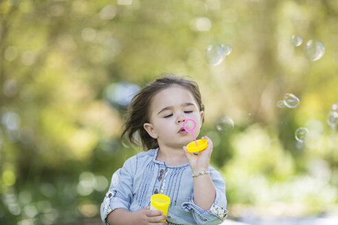 Girl blowing soap bubbles in park - ZEF12357