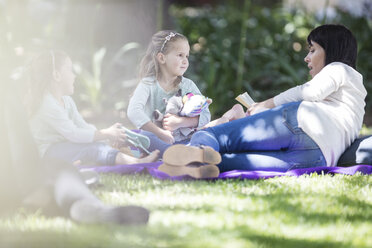 Mother reading a book to children on picnic blanket - ZEF12360