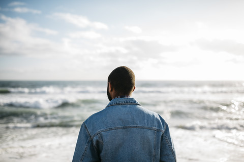 Rückenansicht eines jungen Mannes mit Blick auf das Meer, lizenzfreies Stockfoto