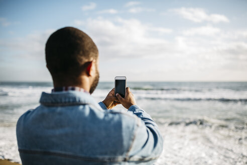 Rückenansicht eines jungen Mannes, der das Meer fotografiert - JRFF01142