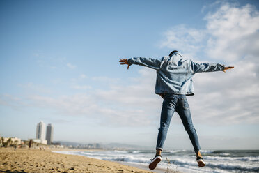 Spain, Barcelona, back view of young man jumping in the air on the beach - JRFF01143