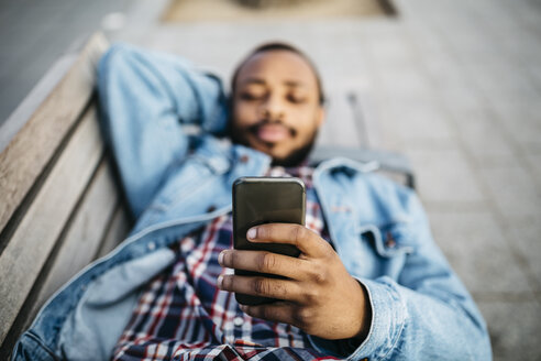 Junger Mann liegt auf einer Bank und schaut auf sein Handy, Nahaufnahme - JRFF01148