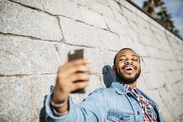 Porträt eines lachenden jungen Mannes, der ein Selfie mit seinem Mobiltelefon macht - JRFF01153