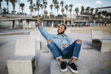 Spanien, Barcelona, lächelnder junger Mann macht Selfie auf der Strandpromenade - JRFF01159