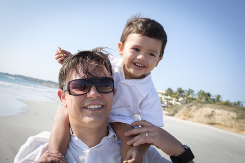 Porträt eines Vaters, der seinen kleinen Sohn am Strand auf den Schultern trägt, lizenzfreies Stockfoto