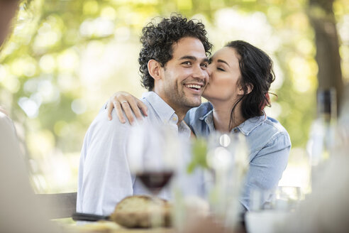 Young woman kissing a happy young man at outdoor table - ZEF12376