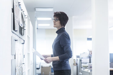 Woman in office looking at notice board - SGF02074