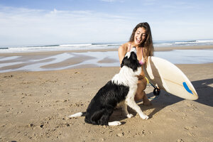 Glückliche Frau mit Hund und Surfbrett am Strand - ABZF01713